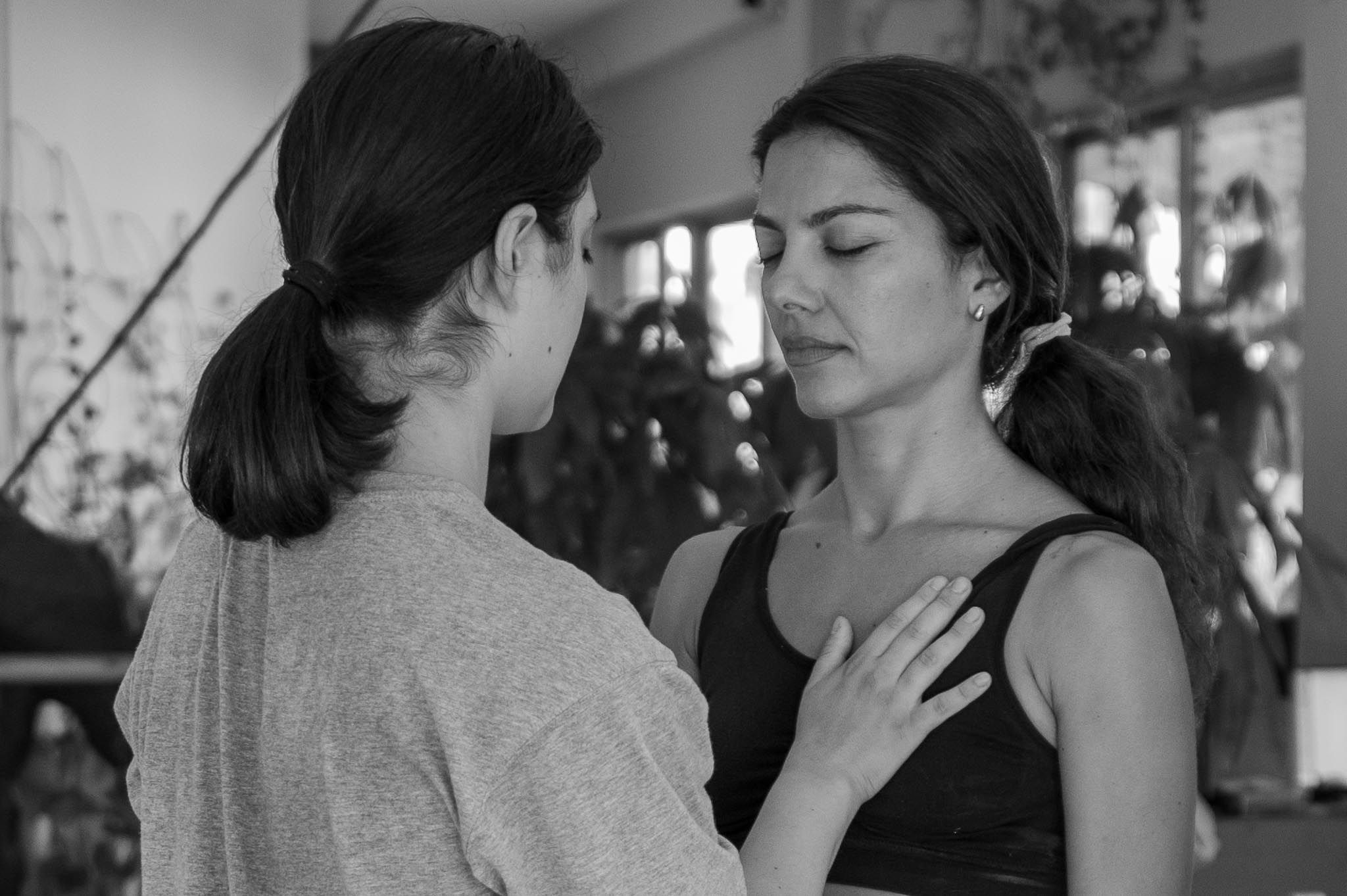Workshop participants standing face to face with eyes closed, one hand placed gently on the other’s chest.